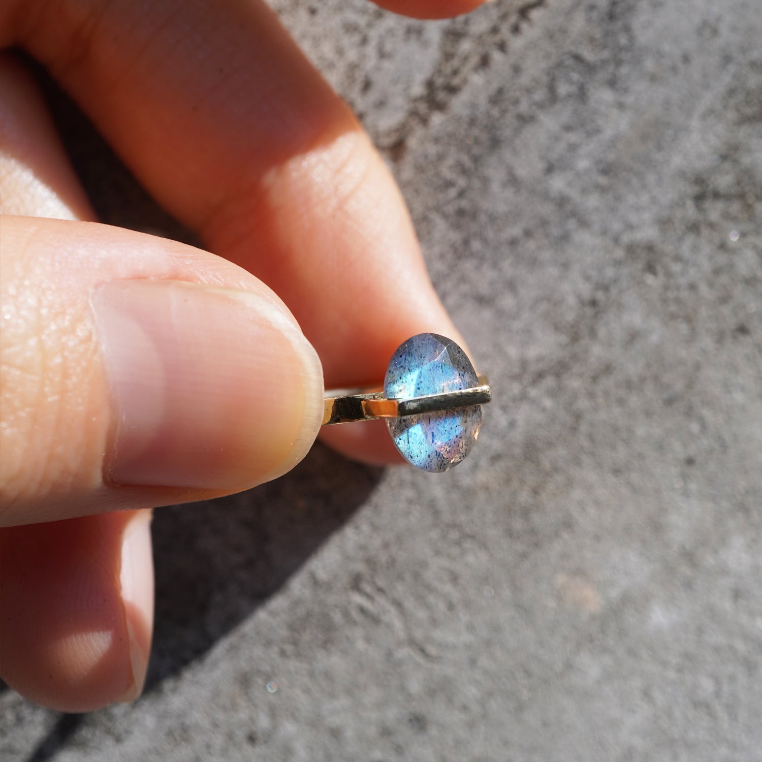 ラブラドライトを使用した指輪を自然光で指で摘んで斜めから見た着用写真。青い遊色効果をしっかりと見れる。