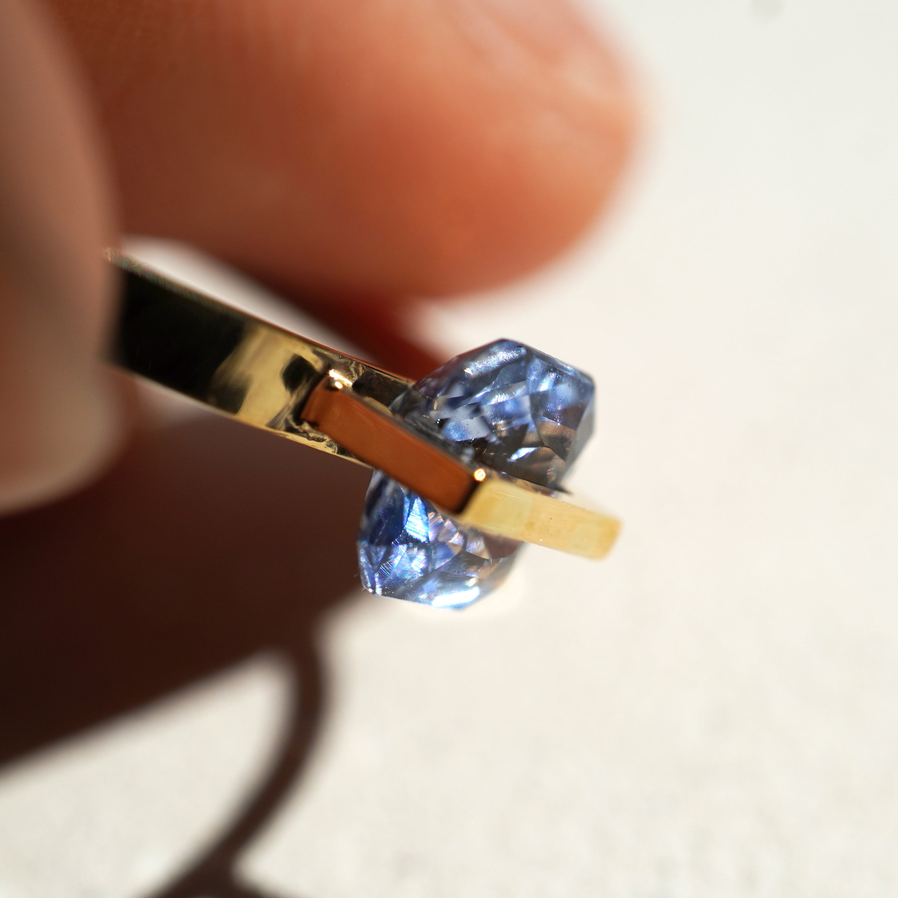 淡めのグレイッシュなブルーのエメラルおカットのサファイアを10金でセッティングしたbandシリーズの指輪を自然光を通してキラキラサファイアが輝いている様子