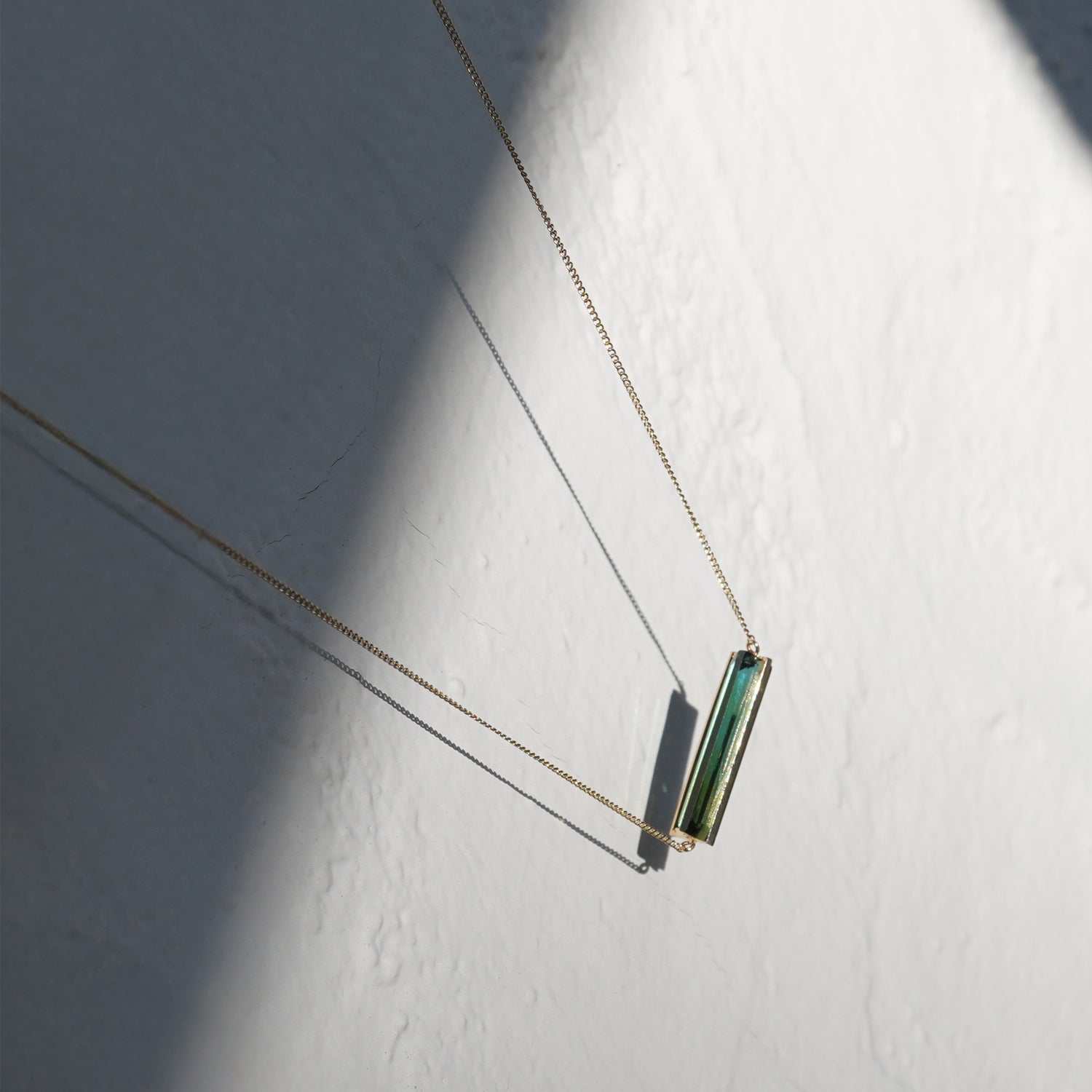 グリーントルマリンの透明感が際立つK10イエローゴールドネックレス、光と影の中で見える縦長バーのフォルム（40cm）
